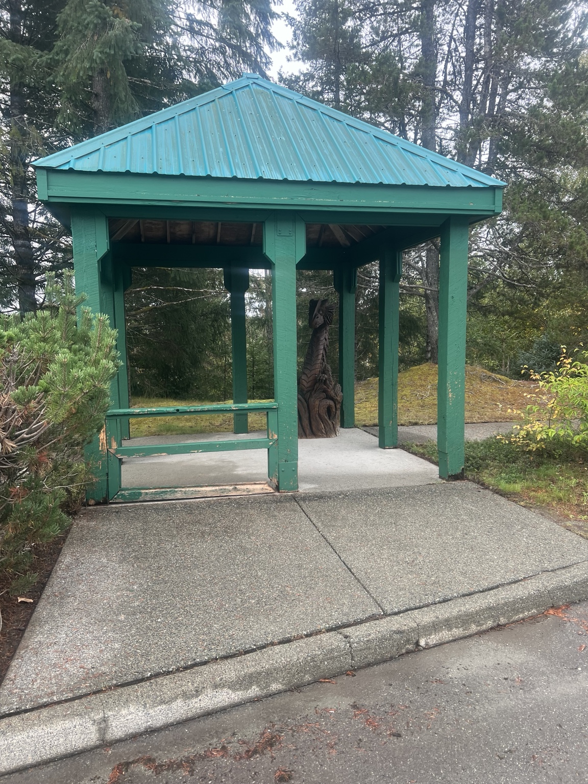 Green wooden shelter with a turquoise roof and carved figure among trees